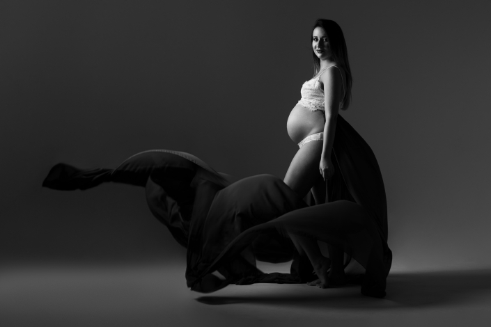zdjęcie kobiety w ciąży na szarym tle pozującej w bieliźnie i z ciemną tkaniną