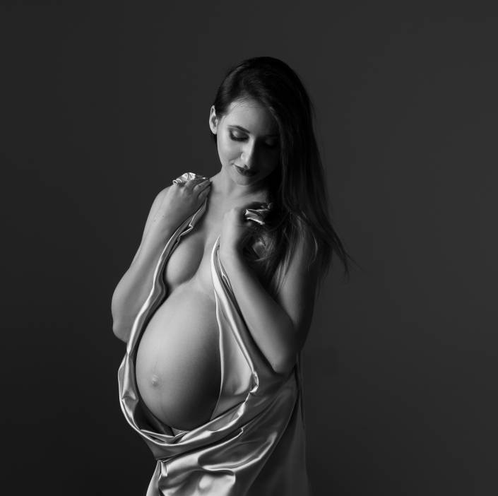 zdjęcie kobiety w ciąży na szarym tle zakrywającej się jasną błyszczącą tkaniną