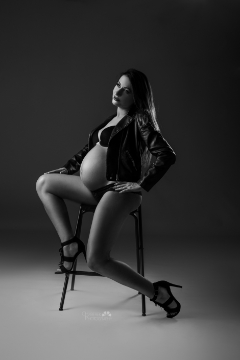 Kobieta z ciążowym brzuszkiem pozująca na wysokim krześle w skórzanej kurtce